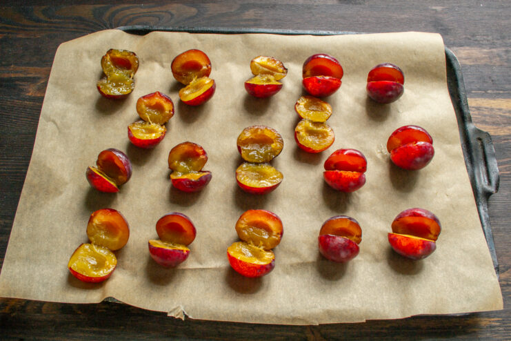 Plum halves evenly arranged on a parchment-lined metal baking sheet