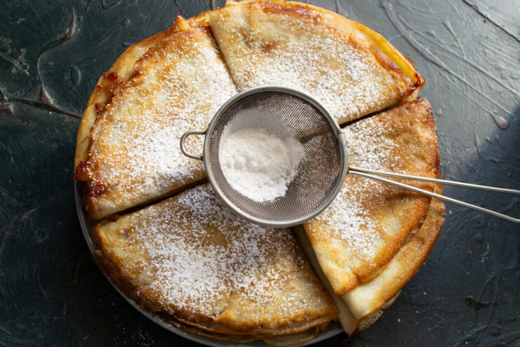 Sprinkling powdered sugar over crepes through a fine sieve