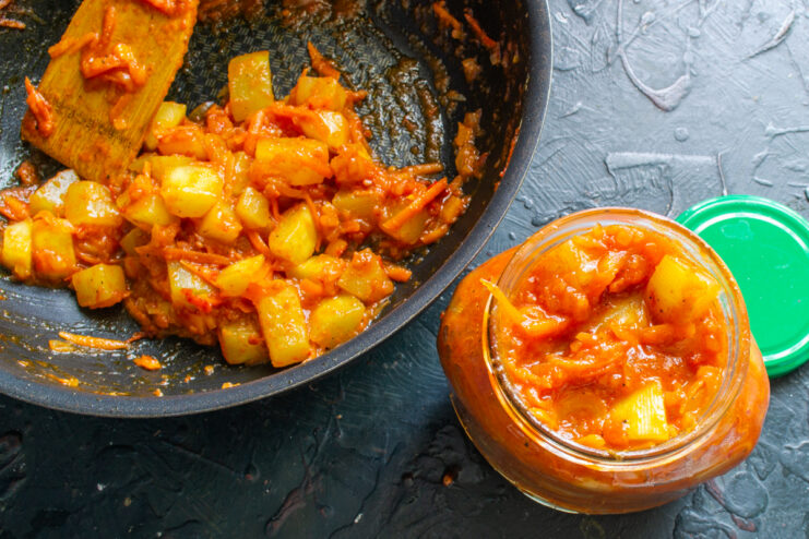 Filling a glass canning jar with hot vegetable sauté