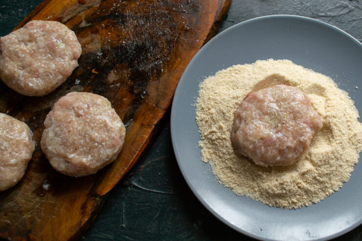 Breading the meat patties Coating a shaped meat patty in breadcrumbs on a plate