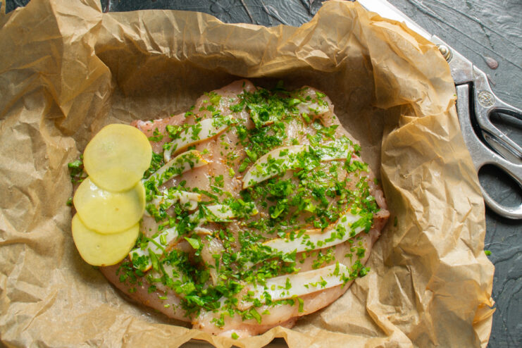 Arranging thin potato slices over the chicken fillet on parchment paper