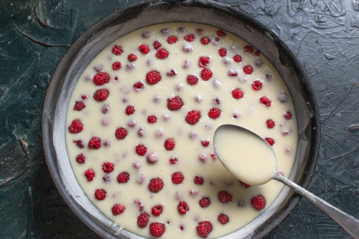 Creating The Layers Spoon pouring a second layer of batter over the fresh raspberries