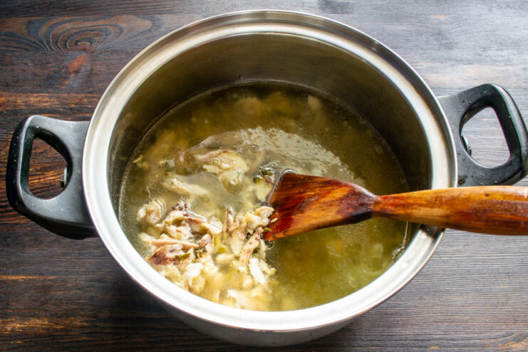 Strained chicken broth being poured over chicken and vermicelli