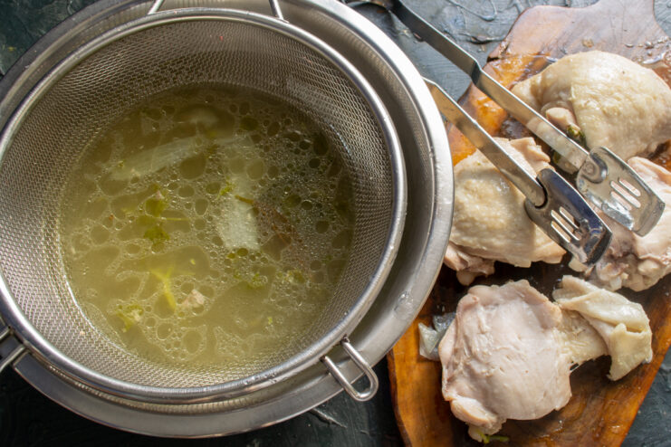 Straining broth and shredding meat Straining chicken broth through a fine-mesh sieve