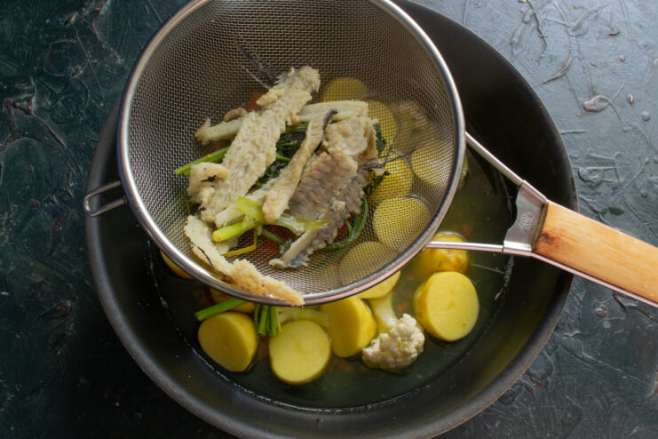 Pouring the broth Straining homemade fish broth through a sieve into a pot filled with vegetables