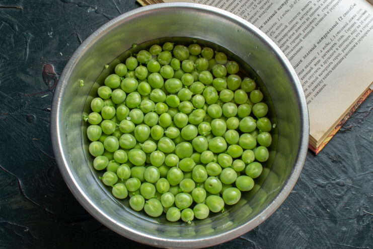 Rinsing shelled green peas in a metal colander under water
