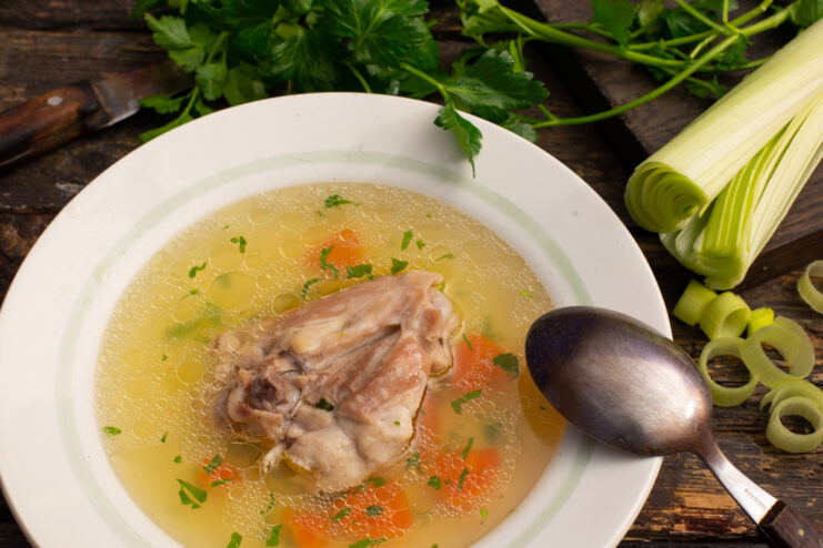 Clear chicken broth with leeks, carrots, and a chicken thigh in a bowl