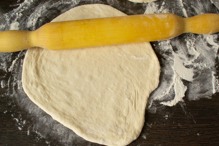 Shaping the pizza base Rolling out pizza dough on a floured table with a rolling pin