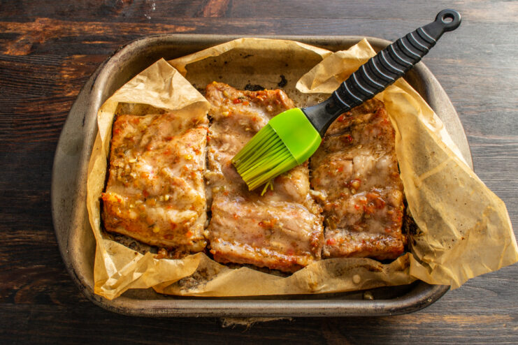 Brushing the honey glaze evenly Spreading honey glaze evenly across baked ribs using a silicone pastry brush.