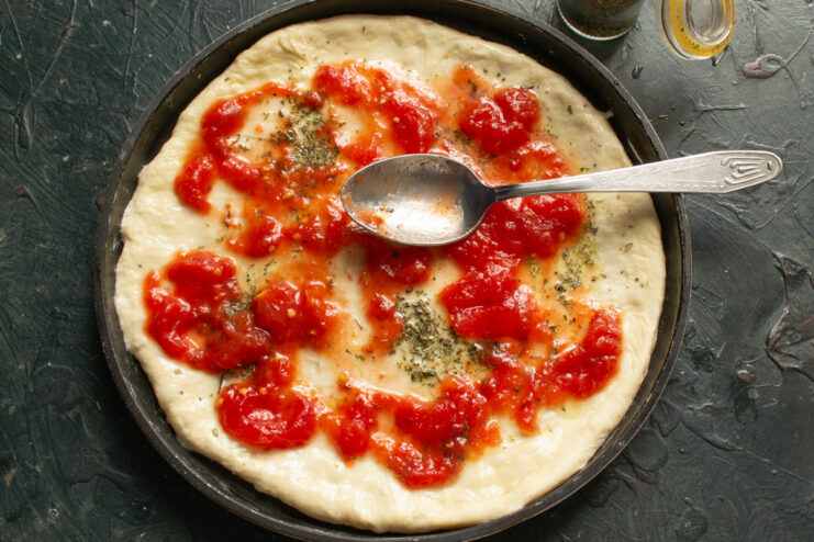 Applying the sauce Spreading tomato puree evenly over the pizza dough