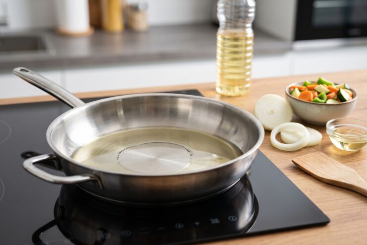 Plant oil heating in a skillet on an induction stove, preparing for frying fresh vegetables.