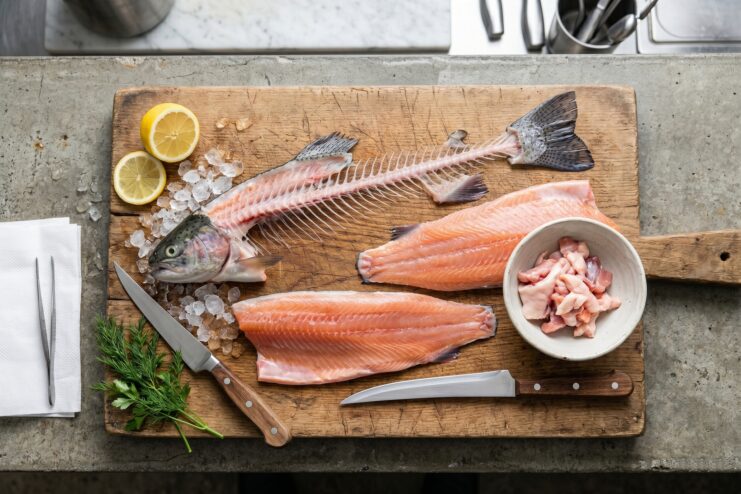 Whole Fish Butchering Results A butchered fish on a wooden board showing the fillet, spine, head, and meat trimmings