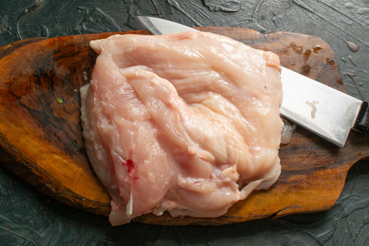 Butterflied raw chicken breast fillet on a wooden cutting board