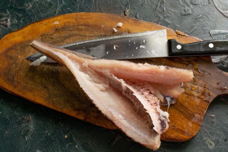 Prepping fish for the soup Butchering a whole fish into fillets on a cutting board to prepare fish broth