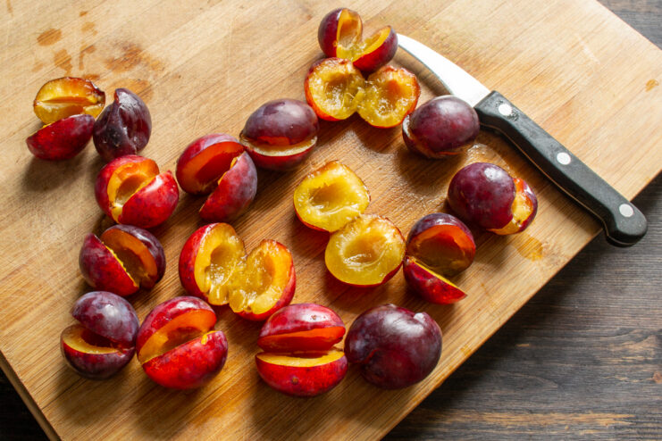 Halved plums with pits removed laid out on a wooden cutting board