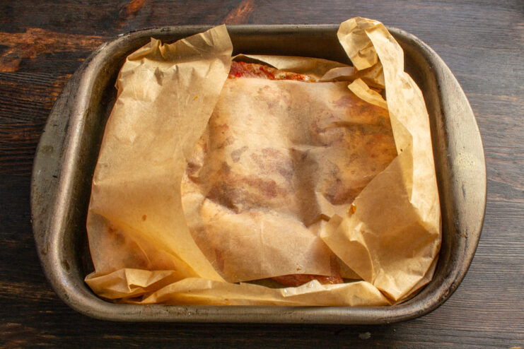 Wrapping the ribs loosely in parchment paper Pork ribs partially covered with folded edges of parchment paper in a baking dish.