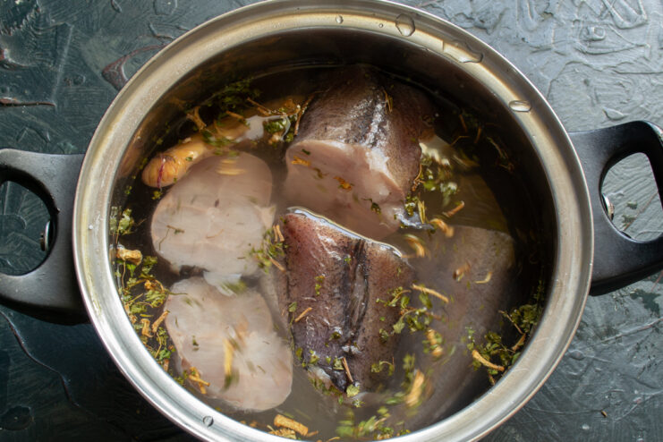 Adding Water to Fish Raw fish chunks covered in cold water inside a metal pot before boiling.