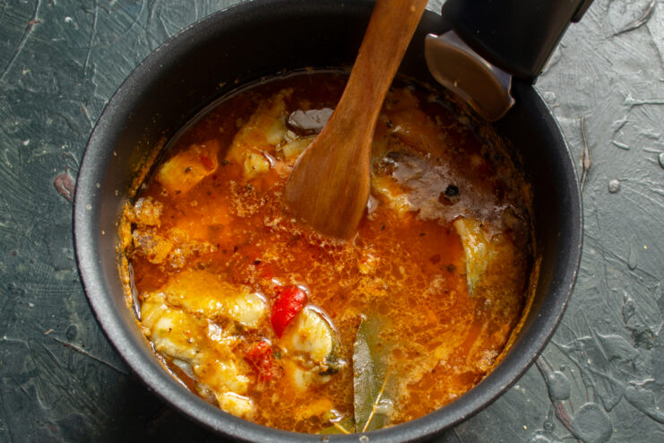 Fish solyanka with a bay leaf simmering in a pot over an open flame.