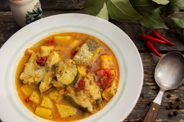 Bowl of vibrant fish solyanka with red bell peppers and spices served on a wooden table.