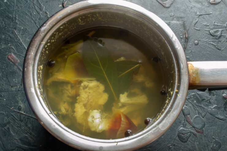 Aromatic fish broth with bay leaves, onion, and peppercorns boiling in a pot.