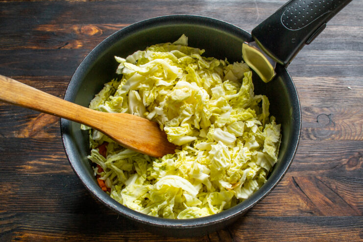 Braising the cabbage Adding shredded Savoy cabbage to sautéed vegetables in a saucepan