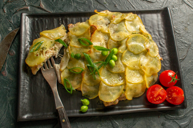 Plated chicken fillet under potatoes on a black plate with a fork