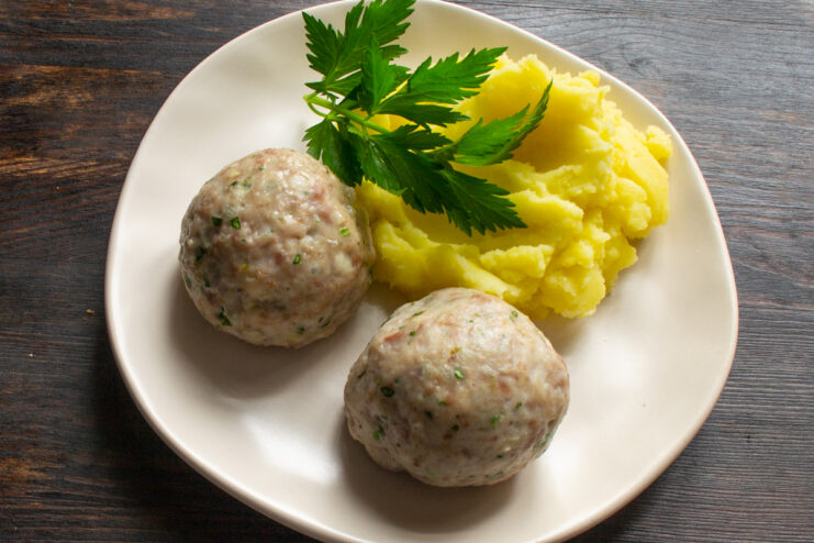 Serving The Dish Serving portion of baked meatballs with mashed potatoes and a sprig of parsley.