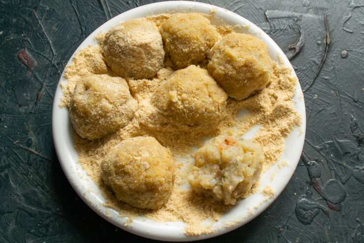 Breading the Fishballs Shaped fishballs coated in breadcrumbs resting on a plate.