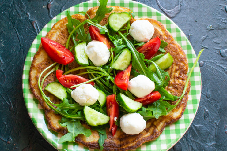 Adding mozzarella cheese Mozzarella pearls on top of an oatmeal pancake with sliced vegetables