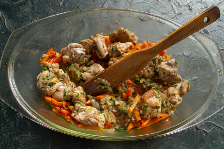 Layering sautéed carrots and spiced chicken in a deep baking dish