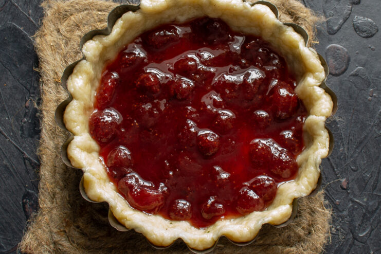 Spreading the strawberry jam filling Thick layer of whole strawberry jam spread evenly over the pie crust.