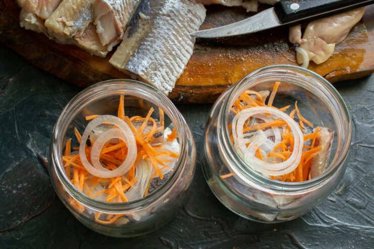 Adding onion and carrot layers Thin onion slices and grated carrot layered on top of the herring in a jar
