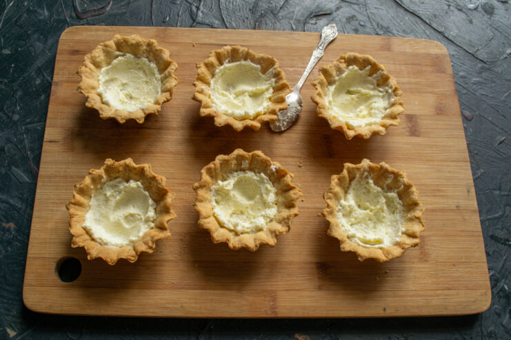 Adding Buttercream Filling Piping a layer of buttercream into the bottom of baked tartlet shells