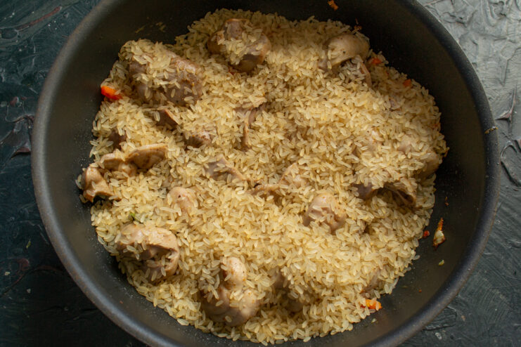 Pouring an even layer of parboiled rice over the meat and vegetables