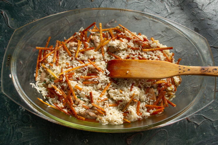 Spreading the toasted rice and noodle mixture evenly over the chicken
