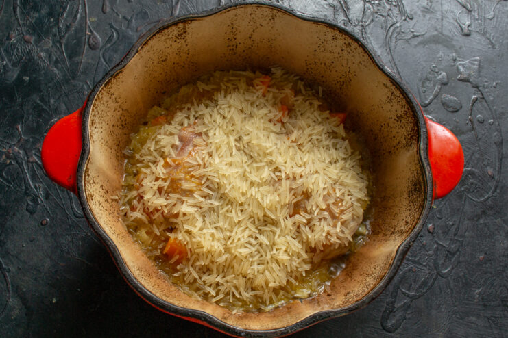 Adding the Basmati rice Layer of dry Basmati rice over chicken and vegetables in a Dutch oven