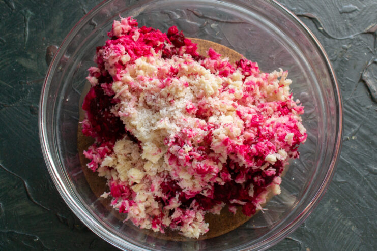 Mixing ground ingredients and salt Mixing freshly ground horseradish, beet, and garlic with salt in a clear bowl.