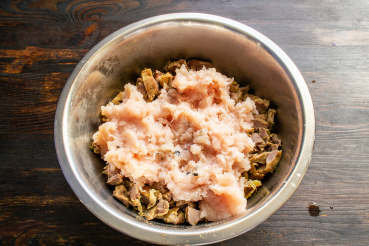 Combining the meats Mixing ground chicken and chopped gizzards in a bowl