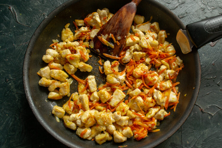 Combining the ragout ingredients Mixing browned chicken pieces with cooked carrots and onions