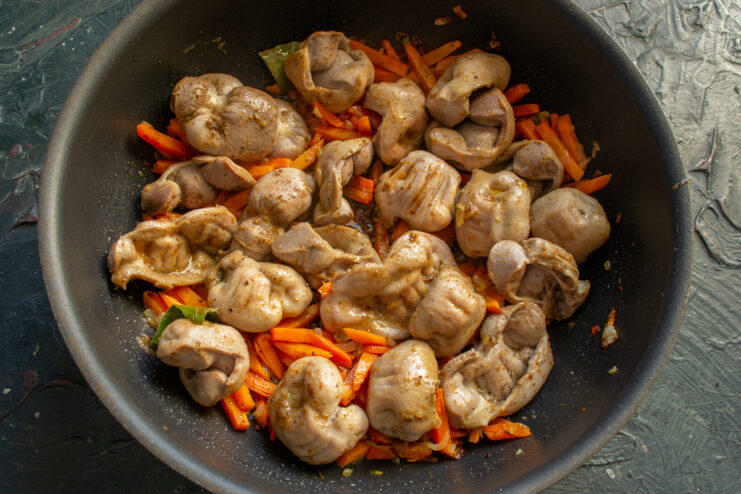 Mixing seared chicken gizzards with browned carrots and onions
