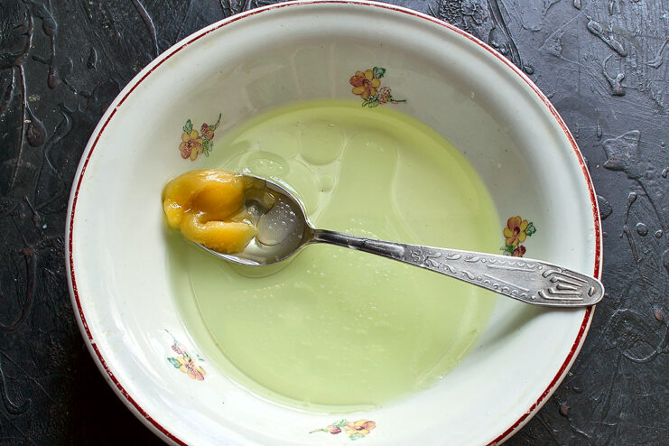 Combining wet ingredients for the dough. Whisking water, oil, and maple syrup or honey in a bowl to make vegan dough base