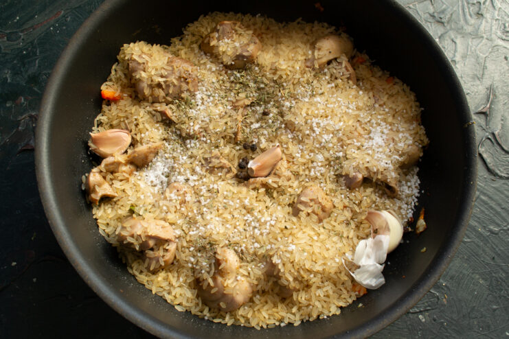 Scattered unpeeled garlic cloves and dried thyme on top of parboiled rice