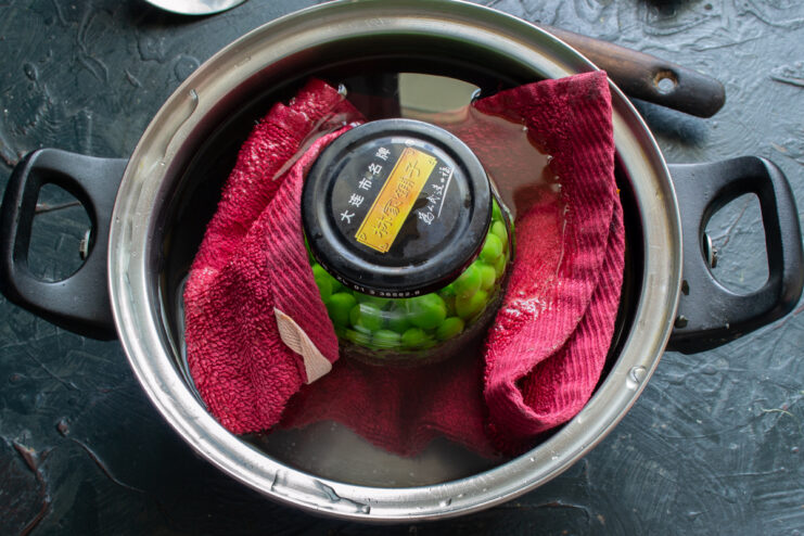 Sterilizing a filled glass jar of peas in a pot of boiling water
