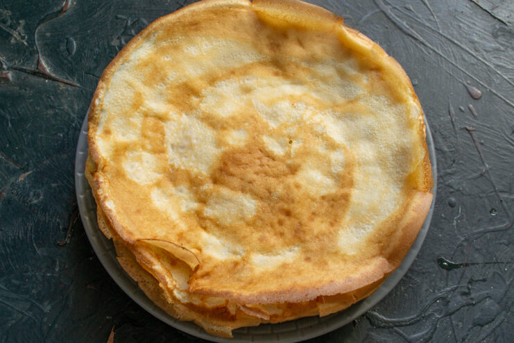 A stack of freshly cooked thin golden crepes