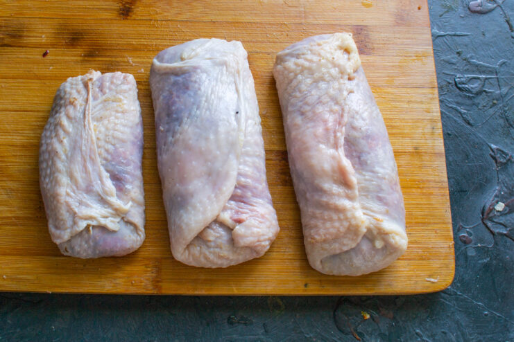 Rolling The Sausages Rolled beef sausages wrapped in chicken skin on a wooden cutting board