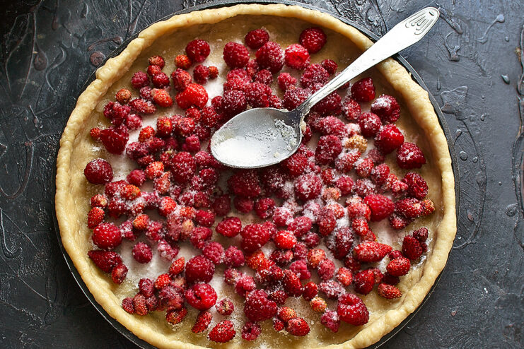 Arranging berries on the dough. Fresh raspberries and wild strawberries spread evenly over the dough base