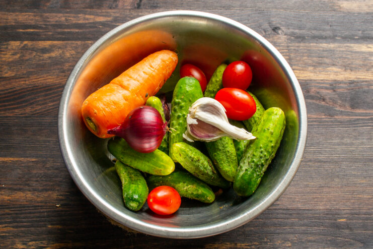 Fresh cucumbers, carrots, cherry tomatoes, and red onions in a metal bowl