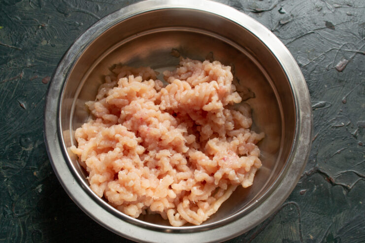 Grinding the chicken fillet Freshly ground chicken meat in a metal bowl