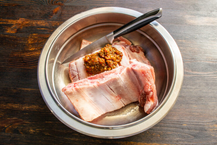 Adding spicy homemade adjika to the meat Pork ribs in a bowl being mixed with spicy homemade adjika paste.