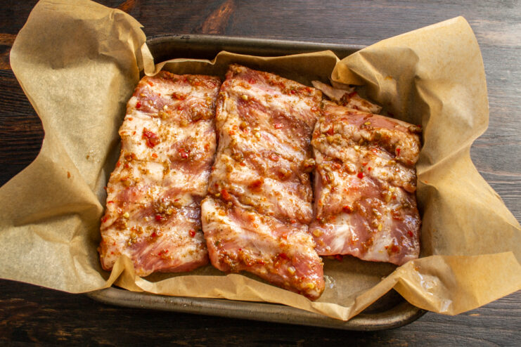 Placing the marinated meat in a baking dish Raw marinated pork ribs laid on parchment paper inside a baking dish.